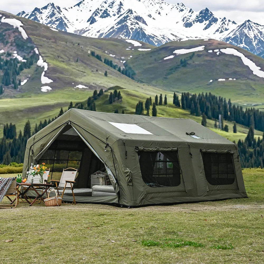 Large green camping tent with outdoor chairs on grassy field, mountains in background