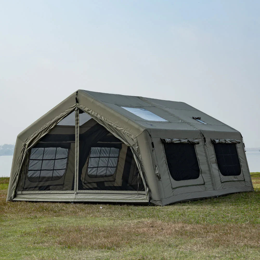 Large khaki canvas cabin tent with multiple windows set up on grass by a lake, camping scene