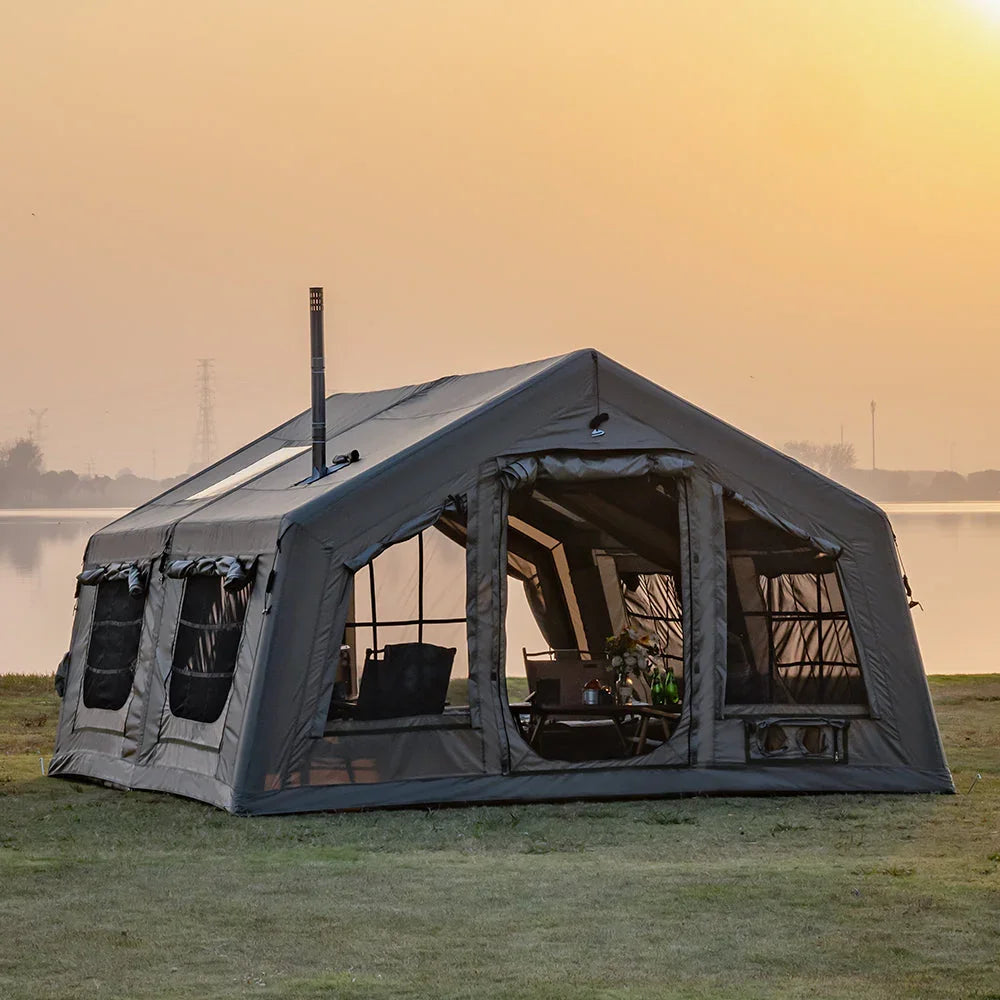 Large camping tent with windows beside a lake at sunset, outdoor gear setup visible inside