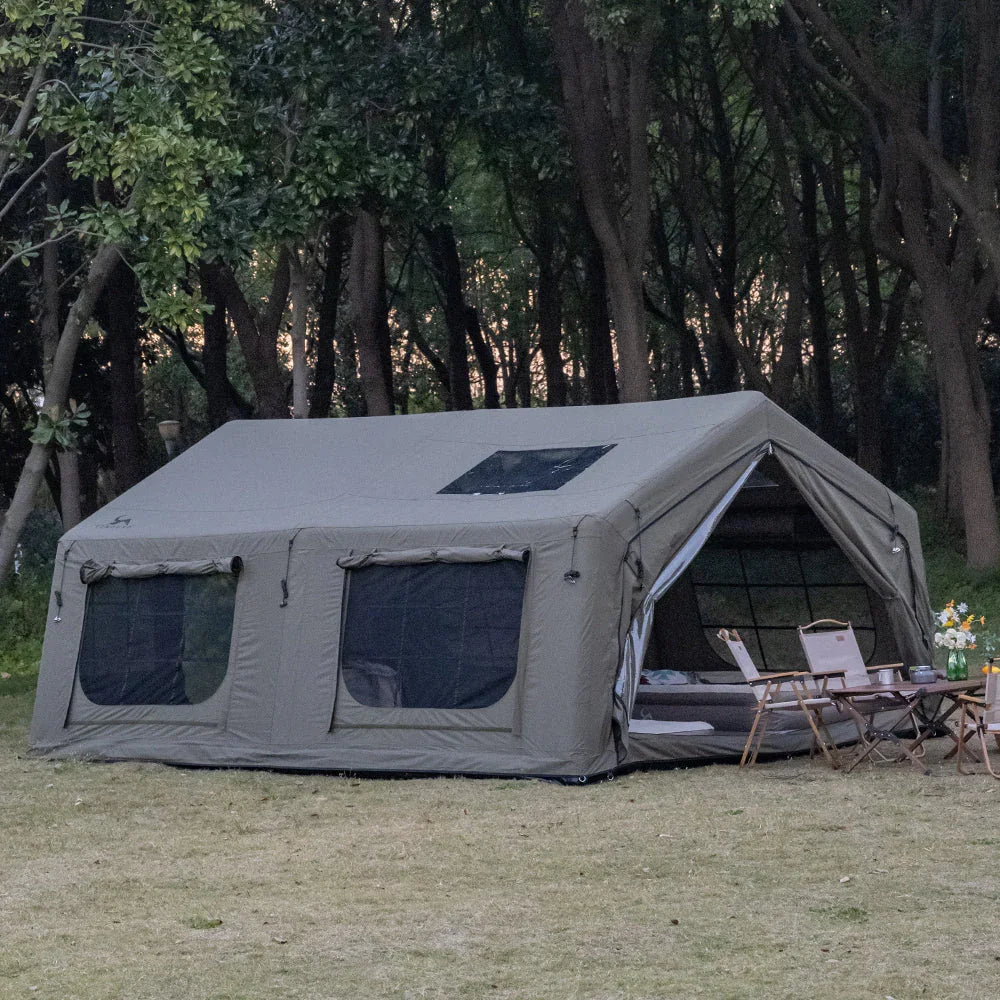 Large canvas camping tent with windows set up in a forest clearing, outdoor chairs and table nearby