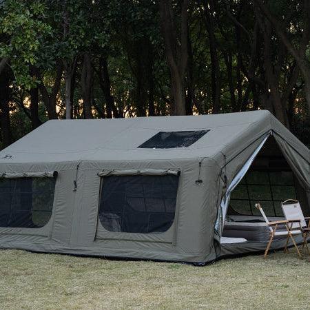 Large canvas camping tent with windows and skylight set up on grass near forest