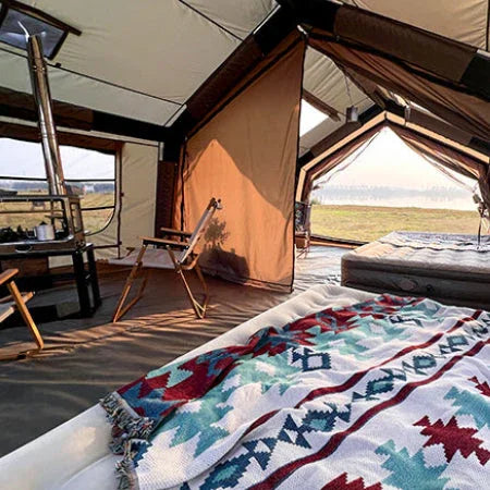 Spacious glamping tent interior with beds, patterned blankets, and outdoor camp chairs