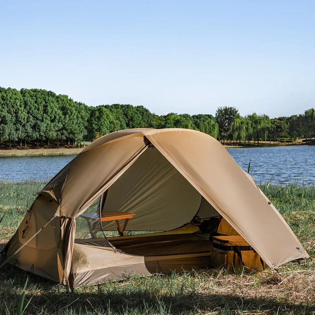 Camping tent set up by a lakeside with trees and clear sky in the background