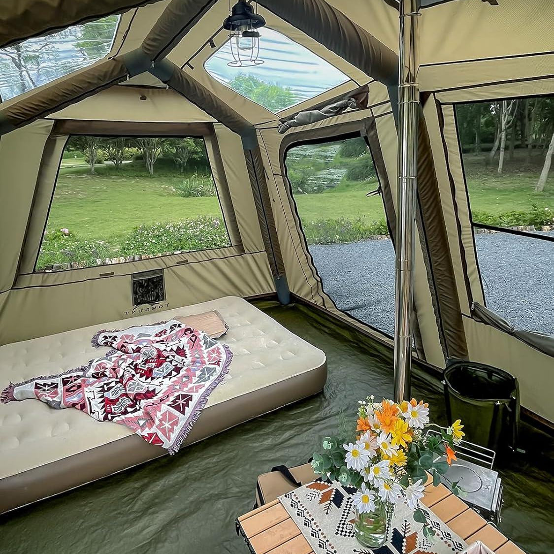 Spacious camping tent interior with mattress, table, flowers, and outdoor view