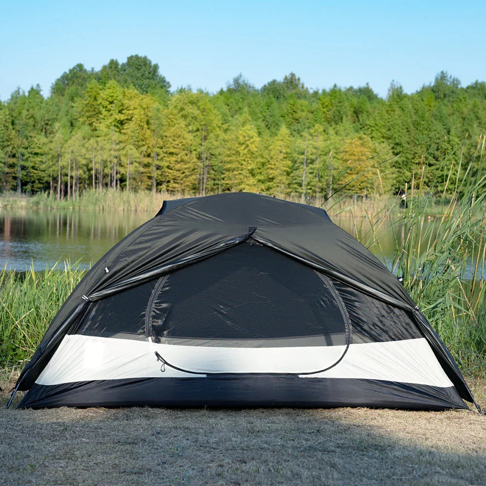 Black and white dome camping tent set up by a lake with trees in the background
