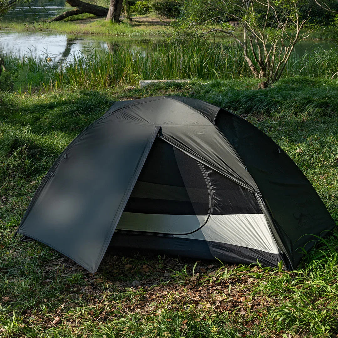 Black dome camping tent set up on grassy lakeside in outdoor nature setting