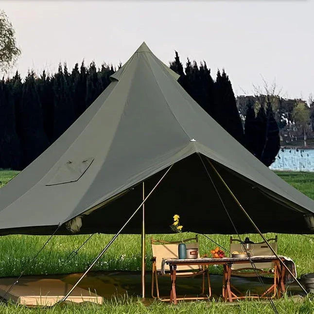 Large green canvas camping tent set up on grass with chairs and table outdoors