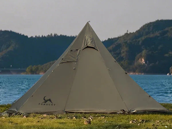 Pyramid camping tent set up by a lake with mountains in the background