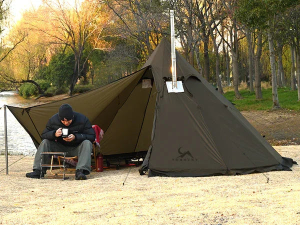Man camping with a large brown tent near a river, surrounded by trees in an outdoor setting.