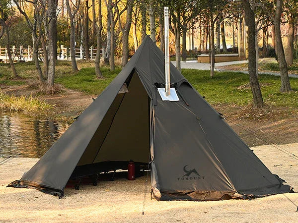 Black tipi camping tent with stove jack setup in a wooded park near a pond