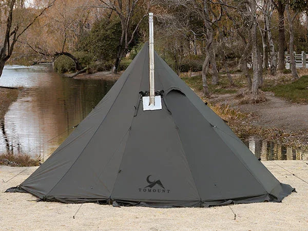 Large green teepee camping tent with stove jack by a river in a forested area