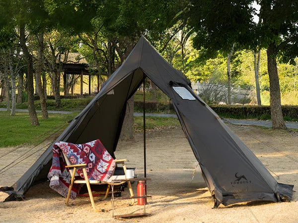 Spacious teepee camping tent set up in a sunny park with chair and outdoor gear
