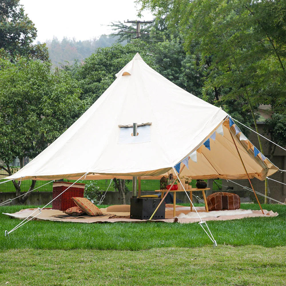 Large canvas bell tent for camping set up on grassy lawn with outdoor furniture and decor