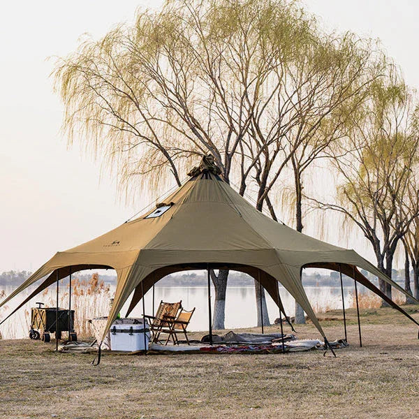 Large camping canopy tent set up by a lake with chairs and camping gear under trees