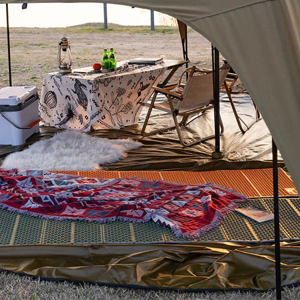 Cozy camping tent interior with picnic table, cooler, chairs and patterned blanket on mat