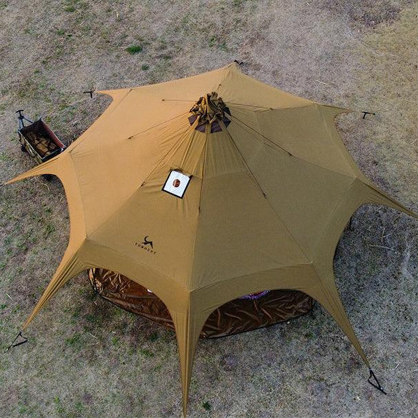 Large brown camping tent with multiple peaks set up on dry grass, viewed from above